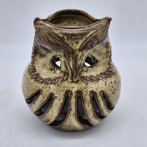 Peut inclure: Un photophore en céramique en forme de hibou, dans des tons de beige et de marron. Le hibou a de grands trous pour les yeux et des motifs découpés sur le bas du corps. Le dessus a une ouverture circulaire pour une bougie.
