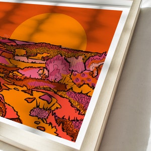 May include: A framed print of a sunset landscape with a large orange sun in the background. The foreground features a stylized landscape with pink, orange, and yellow colors.