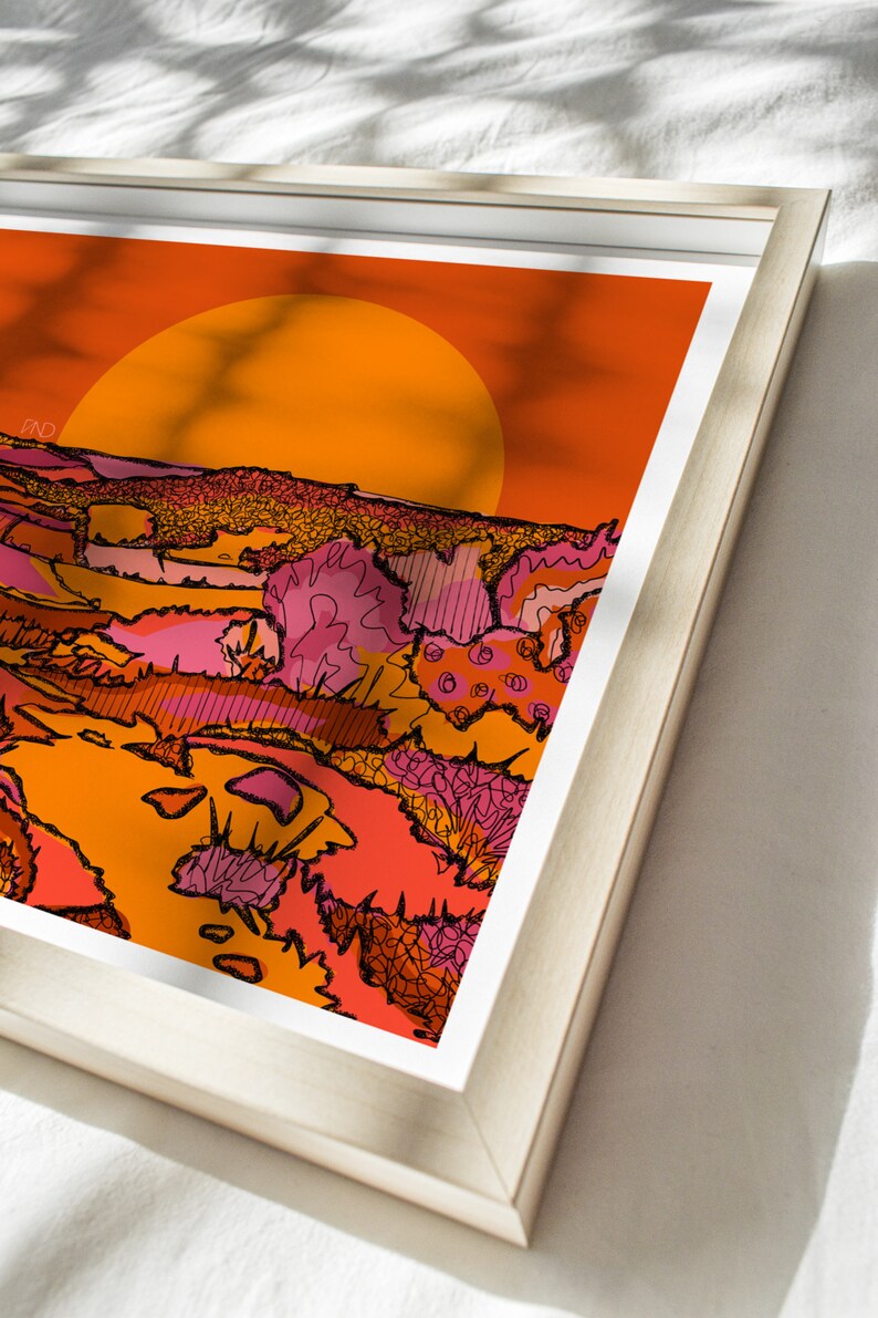 May include: A framed print of a sunset landscape with a large orange sun in the background. The foreground features a stylized landscape with pink, orange, and yellow colors.