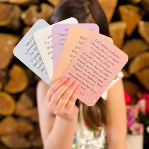 May include: A person holding a fan of prayer cards with inspirational text. The cards are in various pastel colors, including blue, lavender, and peach. The text is in black, and the cards have rounded corners.