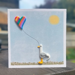 Carte de voeux faite main en pâte polymère avec une mouette et un ballon en forme de coeur arc-en-ciel.