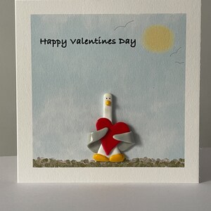 Mouette tenant une carte de voeux en forme de coeur avec des décorations faites main en pâte polymère.