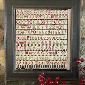 May include: A framed cross-stitch sampler with a white background and green and red embroidery. The sampler includes the alphabet, numbers, and the text "MS-Mary & GSmallx Aged Five Years August 19-1863-East Wemyss".