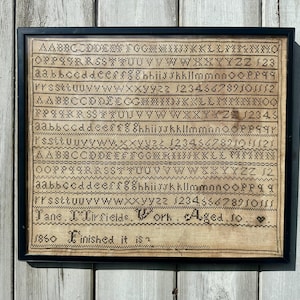 May include: A framed antique sampler with a black frame. The sampler features rows of embroidered letters, numbers, and the text "Jane I. Lirfields. Work. Aged. to. 1850 Finished it is."