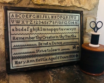 May include: A framed sampler with black embroidery on a cream background. The sampler includes the alphabet, numbers, and the text "Remember thy Creator in thy Youth, Be not a Dunce, Strive to learn, Mary Ann Kettle Aged 8 Years 1838".