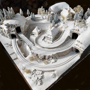 May include: A miniature winter village scene with snow-covered terrain, tunnels, buildings, and a bridge. The model features a winding railway track, evergreen trees, and a detailed landscape, creating a charming diorama.