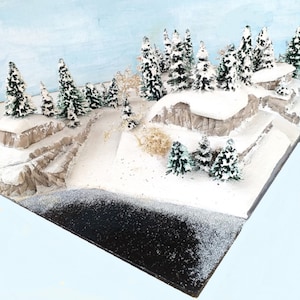 Puede incluir: Un paisaje invernal en miniatura con nieve, un lago congelado y una variedad de árboles de hoja perenne. El paisaje en miniatura está hecho de yeso y pintado con pintura blanca y marrón.