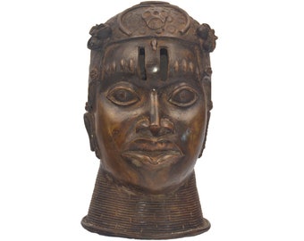 Peut inclure: Une sculpture en bronze d'une tête humaine avec des traits détaillés, notamment de grands yeux, un nez proéminent et des lèvres pleines. La tête est ornée d'une coiffe décorative et d'un collier détaillé. La sculpture a une patine sombre et vieillie.