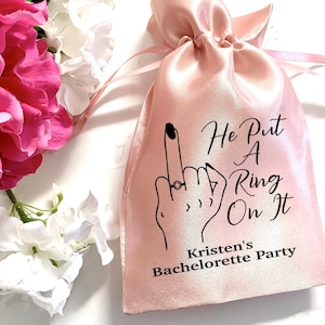May include: Pink satin bag with the text "He Put A Ring On It" and "Kristen's Bachelorette Party" printed on it.