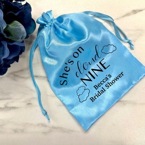 May include: Light blue satin drawstring bag with the text "She's on cloud NINE Becca's Bridal Shower" printed in black.