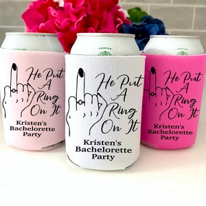 May include: Three pink, white, and black can coolers with the text "He Put A Ring On It" and "Kristen's Bachelorette Party".