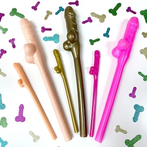 May include: Six colorful plastic straws with a phallic shape. The straws are pink, gold, brown, and green. The straws are on a white background with small, glittery confetti.