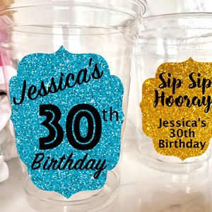 May include: Two clear plastic cups with glitter birthday party decorations. One cup has a turquoise glitter sticker with the text "Jessica's 30th Birthday". The other cup has a gold glitter sticker with the text "Sip Sip Hooray! Jessica's 30th Birthday".