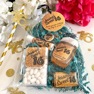 May include: A clear plastic bag filled with party favours for a Sweet 16 birthday party. The bag contains a small bottle of hand sanitiser, a small container of mints, a chocolate bar, and a lip balm. All of the items have gold glitter and the text "Jessica's Sweet 16" on them.