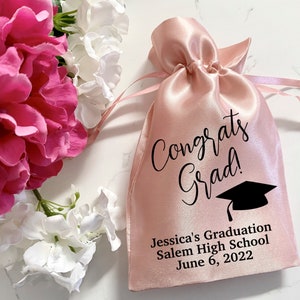 Puede incluir: Bolsa de cord&oacute;n de sat&eacute;n rosa con texto negro que dice "Congrats Grad!" y un gr&aacute;fico de gorro de graduaci&oacute;n negro. La bolsa tambi&eacute;n tiene el texto "Jessica's Graduation Salem High School June 6, 2022".