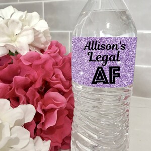 May include: A clear plastic water bottle with a purple glitter label that says "Allison's Legal AF".