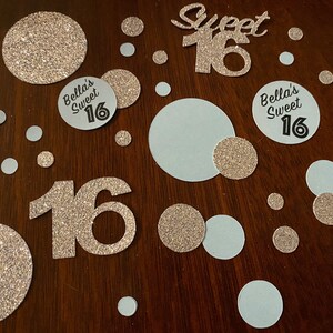 May include: Gold glitter confetti with white and gold circles, and two large gold glitter numbers 16. There are also three circles with the text "Bella's Sweet 16" in black.