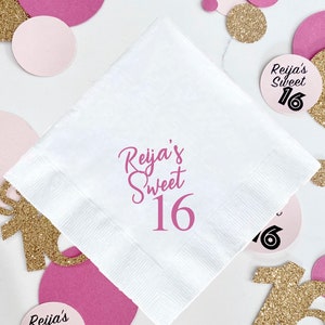 May include: White paper napkin with pink text that says "Reija's Sweet 16". The napkin is surrounded by pink and gold confetti.