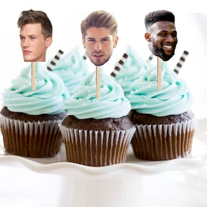 May include: Three cupcakes with blue frosting and chocolate cake topped with edible images of men's faces on sticks.