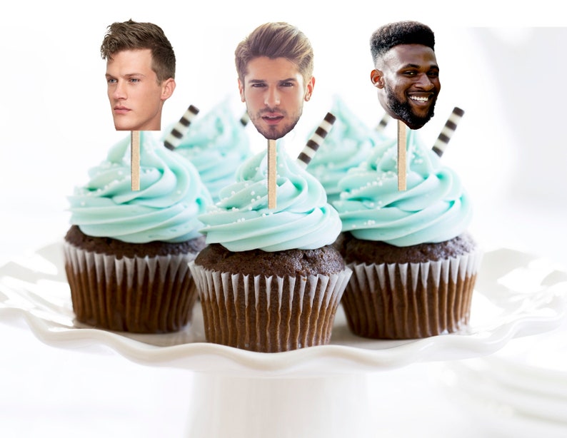 May include: Three cupcakes with blue frosting and chocolate cake topped with edible images of men's faces on sticks.