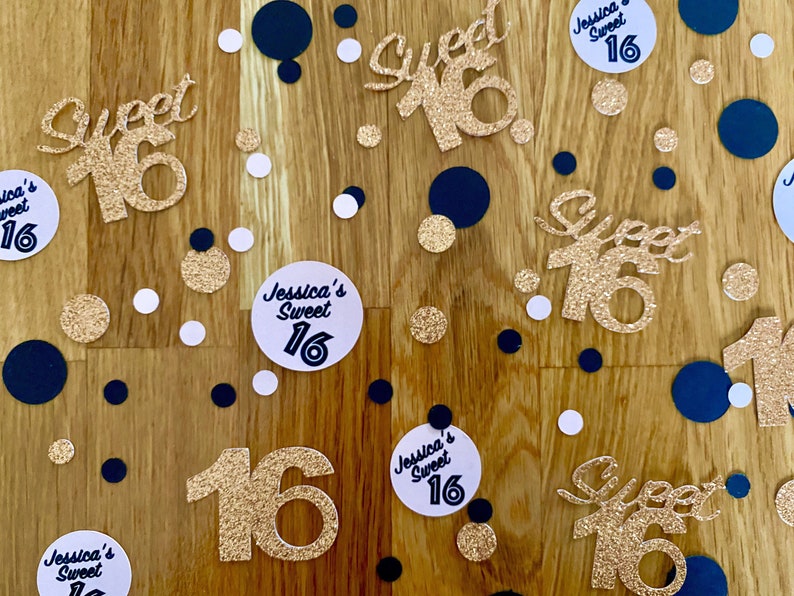 May include: Gold glitter confetti with the words "Sweet 16" and the name "Jessica's" in black lettering. The confetti is scattered on a wooden surface with black and white polka dots.