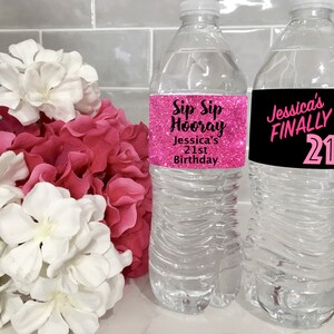 May include: Two clear plastic water bottles with pink and black labels. The labels have text that says "Sip Sip Hooray Jessica's 21st Birthday" and "Jessica's FINALLY 21".