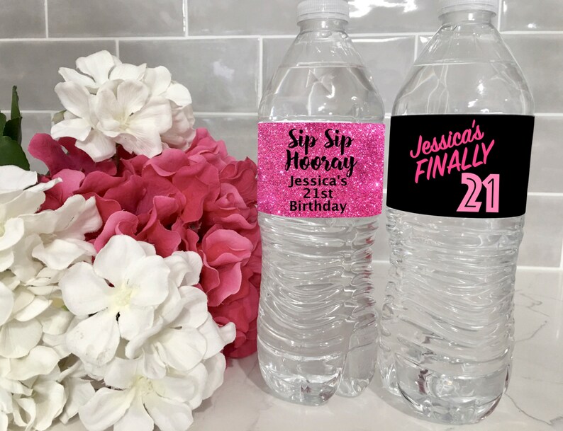 May include: Two clear plastic water bottles with pink and black labels. The labels have text that says "Sip Sip Hooray Jessica's 21st Birthday" and "Jessica's FINALLY 21".