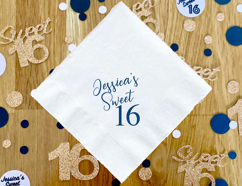 May include: White paper napkin with blue text that reads "Jessica's Sweet 16". The napkin is surrounded by gold and blue confetti.