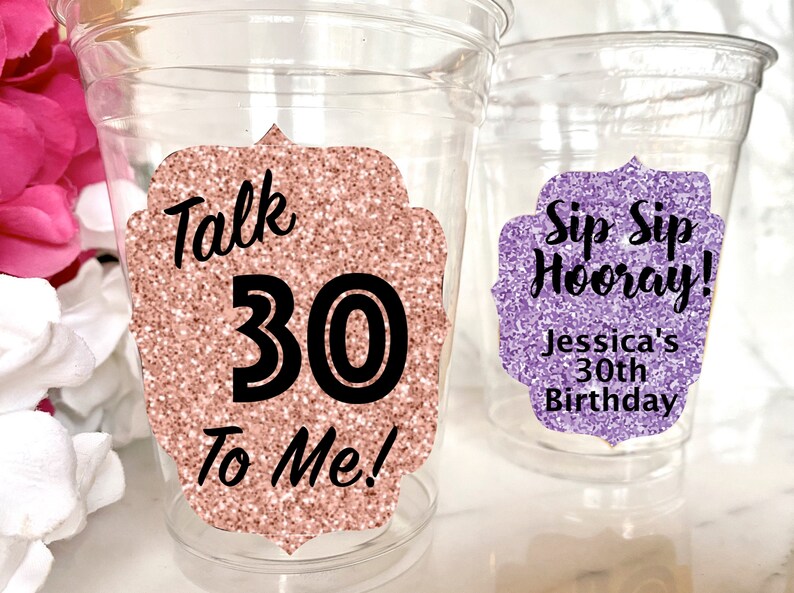 May include: Two clear plastic cups with glitter-covered paper stickers. The pink cup has the text "Talk 30 To Me!" and the purple cup has the text "Sip Sip Hooray! Jessica's 30th Birthday".