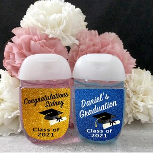 Puede incluir: Dos peque&ntilde;as botellas de desinfectante de manos con etiquetas con tem&aacute;tica de graduaci&oacute;n. La etiqueta dorada dice "Felicidades Sidney Clase de 2021" y presenta un gorro de graduaci&oacute;n y un diploma. La etiqueta azul dice "Graduaci&oacute;n de Daniel Clase de 2021" y presenta un gorro de graduaci&oacute;n y un diploma.