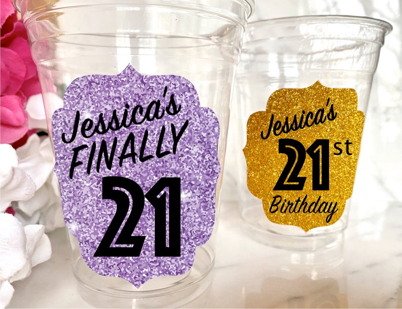 May include: Two clear plastic cups with glitter-covered labels. The purple label says "Jessica's FINALLY 21" and the gold label says "Jessica's 21st Birthday".