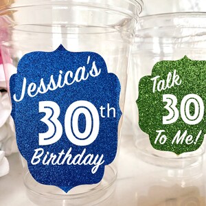 May include: Two clear plastic cups with glitter stickers. The blue sticker says "Jessica's 30th Birthday". The green sticker says "Talk 30 To Me!"