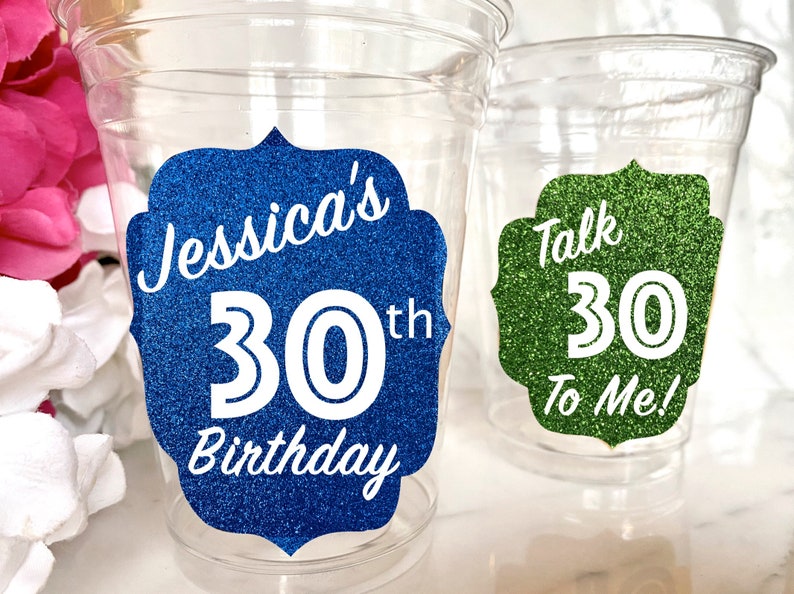 May include: Two clear plastic cups with glitter stickers. The blue sticker says "Jessica's 30th Birthday". The green sticker says "Talk 30 To Me!"