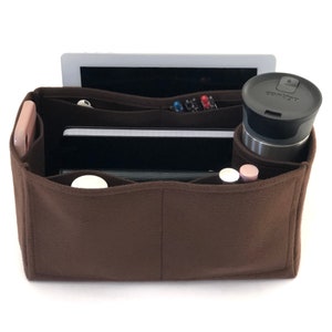 May include: A brown felt handbag organizer with multiple compartments. The organizer is filled with various items, including a tablet, a notebook, a phone, pens, and a travel mug.