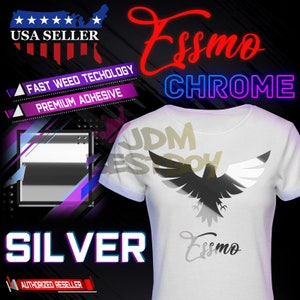 May include: A white t-shirt with a silver chrome eagle graphic on the front. The eagle has wings spread out and is flying. The text "Essmo Chrome" is written in red and blue letters above the eagle. The text "JDM EST SOY" is written in gold letters behind the eagle. The text "SILVER" is written in large white letters at the bottom of the image. The text "USA SELLER" is written in white letters at the top of the image. The text "FAST WEED TECHOLOGY" and "PREMIUM ADHESIVE" are written in white letters on a purple background.