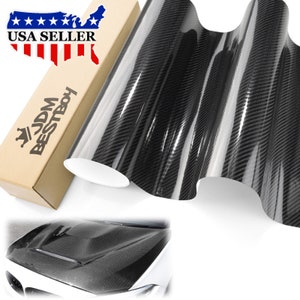 May include: A roll of black carbon fiber vinyl wrap with a glossy finish. The wrap is shown rolled up and partially unrolled, revealing the textured surface. The image also shows a car hood wrapped in the vinyl, showcasing the finished look.
