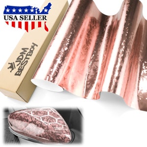 May include: A roll of rose gold chrome vinyl wrap with a textured, brushed finish. The vinyl is shown partially unrolled, revealing the metallic sheen. The vinyl is packaged in a cardboard box with the text "JDM BESTBOY" and "USA SELLER" printed on it.