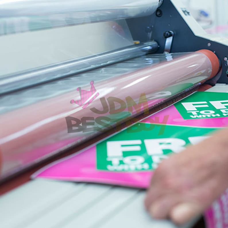 May include: A laminating machine processing a pink and green flyer. The flyer has white text that reads "FREE TO DO WITH". The machine has a large pink roller and clear plastic film.