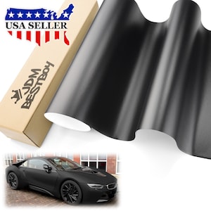 May include: A roll of black matte vinyl car wrap film. The film is shown wrapped around a car, creating a sleek, blacked-out look. The image also includes a box with the text "JDM BESTBOY" and "USA SELLER".