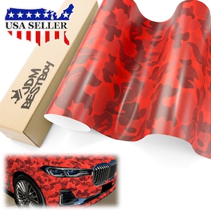 May include: Red camouflage vinyl wrap with a repeating pattern. The wrap is rolled up and a car is partially visible in the background. The car is wrapped in the same vinyl.