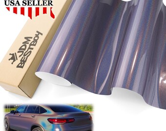 May include: A roll of iridescent vinyl wrap in shades of purple and blue. The vinyl is glossy and reflects light, creating a color-shifting effect. A cardboard box with the text "USA SELLER" and "JDM BESTBOY" is visible.