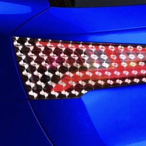 Puede incluir: Primer plano del piloto trasero de un coche azul. El piloto trasero est&aacute; formado por una rejilla de peque&ntilde;as luces cuadradas. Las luces son rojas y blancas.