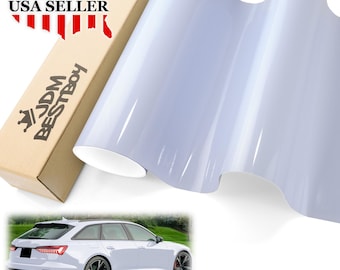 May include: A roll of white vinyl car wrap film. The film is glossy and has a smooth surface. The image also shows a white car with a black grill and black wheels. The text "JDM BESTBOY" is visible on a box in the background.