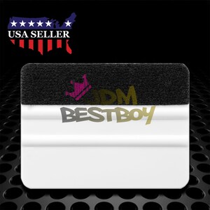 Puede incluir: Rasqueta blanca con un borde de fieltro negro. La rasqueta tiene dos cuchillas y se utiliza para aplicar calcomanías y envolturas de vinilo. La rasqueta tiene el texto "JDM BESTBOY" impreso en ella.