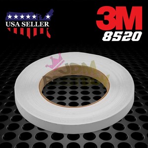 May include: A roll of white 3M 8520 tape. The tape is on a brown cardboard core and is sitting on a black metal surface.