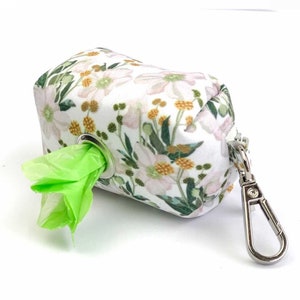 May include: A white floral print dog waste bag dispenser with a green bag dispenser and a silver clip.
