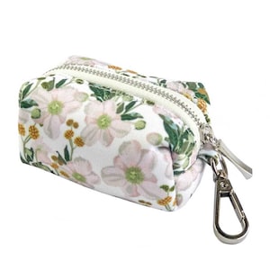May include: A white zippered pouch with a floral print featuring pink flowers, green leaves, and yellow accents. The pouch has a silver metal clip.