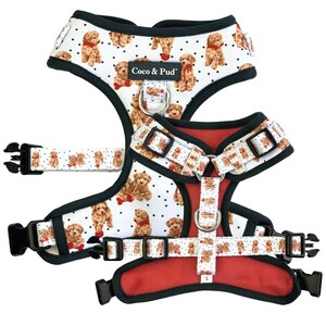 May include: A white and red dog harness with a white and black polka dot pattern featuring a brown poodle with a red bow. The harness has a black adjustable strap and a black buckle. The harness is labelled "Coco & Pud".