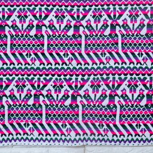 May include: Rectangular textile with a vibrant geometric pattern in white, pink, purple, and black. The design features repeating shapes and figures. The edges are finished with a fringe in shades of green, pink, and purple. This textile is likely a decorative rug or wall hanging.