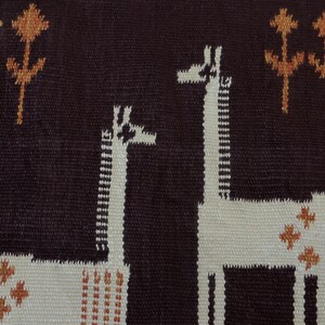 May include: Woven textile featuring two giraffes and stylized trees in brown, cream, and orange. The giraffes have long necks and are set against a dark brown background. The border is cream-colored.